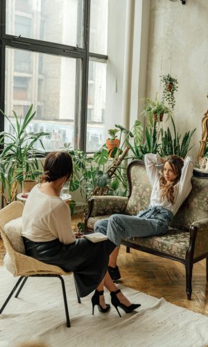 Two women engaged in a counseling session in a cozy, plant-filled living room.